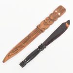 Dois abridores de cartas: a) Um com lâmina em material sintético imitando tartaruga, de coloração variegada em tons castanho e âmbar, acoplada a cabo torneado em baquelite, com fixação por pinos metálicos. b) Em madeira entalhada, de forma alongada, decorado em relevo com motivos geométricos e figura estilizada antropomórfica, com incrustações nos olhos. Medidas: