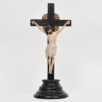 ARTE SACRA. Cristo crucificado. Executado em madeira entalhada e policromada. Cruz latina de hastes retangulares, com acabamento em pintura monocroma escura. Figura de Cristo em vulto pleno, representada com cabeça inclinada, olhos cerrados, perizônio drapeado e marcas da Paixão indicadas por pintura. Resplendor posterior em madeira, em forma de raios estilizados, disposto junto ao cruzeiro. Conjunto fixado em base torneada de perfil escalonado. Estado conforme fotografias. Medidas: Alt.: x Comp.: