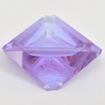 Cinzeiro em cristal de tonalidade lilás, estilo Art Déco, translúcido, com modelagem de caráter geométrico acentuado; estrutura composta por corpo tiriagular facetado, com arestas chanfradas e planos inclinados, formando volume prismático. Centro com cavidade côncava, configurando área de apoio, circundada por reentrâncias angulares destinadas ao descanso de cigarros. Apresenta acentuadas quebraduras. Medidas: