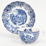 Johnson Brothers, Staffordshire - Inglaterra(Fundada em 1883). Belíssima xícara para chá em faiança inglesa da década de 1960, dotado de profusa decoração em estampagem de tonalidade azul(transferware), sobre fundo com esmaltagem na cor branca. Padrão 'Mill Stream'; retratando paisagem rural contendo casabres, árvores, personagens, moinho d´água e fundo com céu anuviado; bojo hemisférico moldado com sucessão de frisos ondulados, relevados na própria pasta, padrão decorativo integralmente replicado no pires, com orla igualmente modelada e preenchida com flores e folhagens, borda recortada. Marca da manufatura no verso do pires. Medidas.: Xícara: Alt.: 6,5 x Comp.: 12 x Larg.: 10 cm; Pires: Diam. 16 cm.