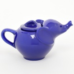 Bule zoomorfo em cerâmica esmaltada, manufatura Elephant (Elephant Pottery Co.), Japão, segunda metade do século XX. Corpo globular conformado em figura de elefante, com bico vertedor integrado à tromba e tampa destacável moldada com orelhas; alça posterior em arco aplicada. Superfície integralmente revestida por esmalte vítreo monocromático azul cobalto, com acabamento brilhante. Base com marca em relevo representando cabeça de elefante e inscrição ELEPHANT. Medidas: