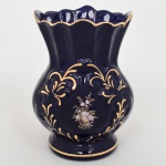 Vaso em cerâmica moldada, esmaltação monocromática e decoração aplicada em douração e policromia; corpo bojudo com cintura estrangulada e colo alargado, borda ondulada, base circular com filete dourado, superfície em esmalte azul cobalto, decoração em relevo com volutas e motivos vegetalistas, reservas com composição floral em policromia e aplicações em douração na borda e ornatos. Medidas