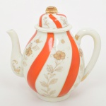 Bule para café em porcelana japonesa, bojo oval assentado sobre base circular, bico vertedor curvilíneo e asa lateral em arco. Tampa campaniforme com encaixe interno e pega superior moldada em dupla folhagem. Esmaltação de tom marfim, dotada de decoração em reservas verticais alternando faixas onduladas em esmalte vermelho-coral e painéis com motivos florais estilizados em douração linear, distribuídos de forma contínua pelo corpo e tampa; realçado por generosos arremates de filetes dourados acompanhando bordas, bico e contorno da asa.Marca em esmalte na base com inscrição "MARCA REGISTRADA - KKR -  MADE IN JAPAN", indicando produção japonesa de exportação. Medidas: Alt.: 18 x Comp.: 18 x Larg.: 12,5 cm. Apresenta perda da douradura da alça.