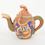 Excepcional bule para chá em porcelana japonesa, decoração policroma, aplicação moriage em relevo, generosos arremates em pintura à ouro; bojo oval ornamentado com composição figurativa, formada por deidade central sentada, acompanhada por quatro Imortais(sennin/rakan), representando anciãos em trajes tradicionais, tema recorrente em produções de exportação em estilo Satsuma, fundo preenchido por padrão de ondas, com áreas delimitadas por contornos dourados. Pega da tampa, bico vertedor e alça lateral modelados em forma de dragão, dando a impressão do dragão estar atravessando o bojo de um lado para o outro. A iconografia e a técnica de moriage situam a peça dentro da produção japonesa voltada ao mercado externo entre o final do período Taisho e o início do período Showa. Fundo apresenta marca de manufatura com caracteres japoneses em vermelho-ferro. Medida: Alt.: 20,5 x Comp.: 14 x Larg.: 14 cm.