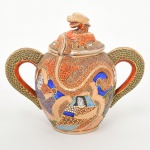 Excepcional açucareiro em porcelana japonesa, decoração policroma, aplicação moriage em relevo, generosos arremates em pintura à ouro; bojo oval ornamentado com composição figurativa, formada por deidade central sentada, acompanhada por quatro Imortais(sennin/rakan), representando anciãos em trajes tradicionais, tema recorrente em produções de exportação em estilo Satsuma, fundo preenchido por padrão de ondas, com áreas delimitadas por contornos dourados. Pega da tampa, e alças laterais modelados em forma de dragão, dando a impressão do dragão estar atravessando o bojo de um lado para o outro. A iconografia e a técnica de moriage situam a peça dentro da produção japonesa voltada ao mercado externo entre o final do período Taisho e o início do período Showa. Fundo apresenta marca de manufatura com caracteres japoneses em vermelho-ferro. Medida: Alt.: 16 x Comp.: 18,5 x Larg.: 12 cm.