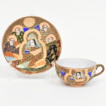 Belíssima xícara para chá em porcelana japonesa com decoração policroma, aplicação de moriage em relevo, realces em ouro e filete na borda. Apresenta composição figurativa formada por uma figura central sentada, acompanhada por quatro Imortais (sennin/rakan), representados como anciãos em trajes tradicionais, tema recorrente em produções de exportação em estilo Satsuma. O fundo do campo decorativo é preenchido por padrão de ondas, com áreas delimitadas por contornos dourados. O verso possui marca em losango contendo a inicial "H" insira em reserva losangular acompanhada de caracteres, identificação utilizada na porcelana japonesa de exportação a partir do início do século XX. A iconografia e a técnica de moriage situam a peça dentro da produção japonesa voltada ao mercado externo entre o final do período Taisho e o início do período Showa. Medidas