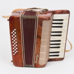 Acordeão de teclado, marca Hering, com corpo revestido em material sintético marmorizado em tonalidade rubra. Teclado lateral composto por teclas retangulares em material plástico, alternando naturais e sustenidos. Lado oposto com botões circulares dispostos em fileiras paralelas. Fole central em tecido sanfonado, com dobras estruturadas e terminais reforçados.Grade frontal metálica perfurada, com padrão geométrico regular, protegendo o conjunto de vozes. Inscrição Hering aplicada na parte frontal. Estrutura com ferragens aparentes e elementos de fixação. Acompanha alças em material sintético para sustentação. Medidas: