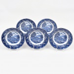Conjunto de pratos rasos em faiança inglesa decorado em esmalte monocromático azul sob vidrado sobre fundo branco, pertencente ao padrão denominado Old Castle. A decoração apresenta, no medalhão central, uma paisagem idealizada de caráter pastoral, com edificação senhorial ao fundo, ponte arqueada sobre curso dágua, vegetação arbórea e céu anuviado, composição inspirada nas paisagens românticas europeias frequentemente utilizadas na cerâmica inglesa; aba circundada por frisos em movimento onduiado, relevado na própria pasta, ricamente ornamentada com bordadura floral estilizada, composta por flores, ramos e elementos vegetalistas entrelaçados, delimitada por filetes ondulados e pontilhados, característica típica da tradição decorativa da cerâmica de Staffordshire. Verso com marca impressa em azul com a inscrição OLD CASTLE  by Barratts of Staffordshire Ltd., acompanhada das menções Acid and Detergent Proof e Genuine Hand Engraving, além da identificação do estúdio R. Kirkham  P. Boardman, indicando o ateliê responsável pela gravação do desenho original utilizado na impressão transferida da decoração. Produção inglesa destinada ao mercado doméstico e de exportação, representativa da tradição cerâmica de Staffordshire, região historicamente associada à produção industrial de louças decoradas desde o século XVIII. Composto de seis(06) unidades. Medida: Diam.: 23 cm.