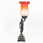 Abajur com figura feminina e cúpula em vidro acetinado. Estrutura em metal fundido, representando figura feminina em vulto pleno, com drapeado aderente ao corpo, apoiada sobre base escalonada. Braço elevado sustentando suporte superior para cúpula. Superfície com acabamento escurecido. Cúpula em vidro acetinado moldado, de perfil campaniforme, com bordo ondulado e transição cromática em degradê, do branco ao vermelho. Estado de conservação com desgaste generalizado do acabamento com abrasão e perdas pontuais. Parte elétrica não está funcionando. Demanda restauro. Medidas: