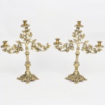 Par de candelabros de três luzes confeccionado em bronze, e metal dourado, com estrutura em haste central balaustrada, encimada por ramificações simétricas em volutas. Braços e hastes ornados por folhas de carvalho e bolotas em relevo, formando composição fitomórfica contínua. Bocas com colarinhos em forma de folhas estilizadas. Base recortada com pés integrados e decoração vegetal em relevo. Medidas: Alt.: x Comp.: x Larg.: