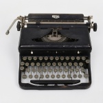 Máquina de escrever mecânica portátil da década de 1930/40,  marca Royal Typewriter Co., Inc., New York, com corpo em metal pintado em preto. Teclado alfanumérico com disposição QWERTY, teclas circulares com tampas em vidro e anéis metálicos, incluindo tecla de maiúsculas. Carro superior com régua graduada e manípulos laterais para avanço e retorno, além de alavanca de retorno à esquerda. Mecanismo interno visível sob tampa articulada. Base retangular com pés de apoio, estrutura compacta característica dos modelos portáteis da marca. Inscrição no verso: Royal Typewriter Co., Inc. New York. Made in United States of America. Protected by American and Foreign Patents. Medidas: Alt.: x Comp.: x Larg.: