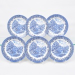 Conjunto de pratos rasos  em faiança inglesa esmaltada, decorado em esmalte monocromático azul sob vidrado sobre fundo branco, medalhão central apresenta cena pastoral campestre, com personagens em atividade agrícola, colheita de cereais e paisagem arborizada ao fundo, composição de inspiração bucólica típica da tradição decorativa inglesa, aba ornada por bordadura floral estilizada com elementos vegetalistas e espigas de trigo, formando composição contínua em azul cobalto que remete aos padrões tradicionais da cerâmica inglesa decorativa produzida em Staffordshire. Verso com marca impressa Churchill  England, acompanhada da figura de leão heráldico, além da indicação Dishwasher & Microwave safe, denotando produção industrial contemporânea destinada ao uso doméstico. Fundada em 1795 em Staffordshire, é uma tradicional manufatura inglesa de louças e porcelanas, amplamente reconhecida pela produção de serviços de mesa e peças decorativas com inspiração nos clássicos padrões da cerâmica britânica. Composto de seis(06) unidades. Medida: Diam; 24,5 cm.