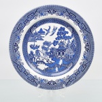 Churchill,  Stoke-on-Trent - Inglaterra. Prato de coleção em faiança inglesa, decoração na técnica "blue and white", padrão salgueiro, estilo chinoiserie, composição central composta por salgueiros, pagodes, ponte sobre o rio, embarcação, pássaros e personagens. Padrão conhecido pelo senso comum como "azul pombinho". Marca da manufatura no verso. Medida: Diam.: 26,5 cm.