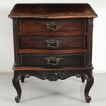 Belíssima mini-cômoda construída em madeira nobre, estilo Luis XV; tampo recortado de contorno ondulado, frente abaulada, laterais em painéis rebaixados, montantes com entalhes florais, três gavetas sobrepostas com frentes sinuosas e ferragens em metal, vazado e cinzelado; saia recortada com elemento central esculpido, apoiada sobre quatro pés em cabriole com terminação de enrolamento. Medidas: Alt.: 53 x Comp.: 48 x Larg.: 38 cm.