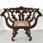 Poltrona em madeira maciça, com espaldar recortado e vazado, composto por elementos entalhados em volutas e motivos vegetalistas estilizados, coroamento superior com cartela central em concha, braços curvos com terminações enroladas e apoios entalhados, assento retangular com rebaixo e trama em palhinha natural, sustentada por estrutura inferior com pernas recortadas e interligadas por elementos vazados e entalhados, com pés em voluta. Produção provavelmente brasileira, datável do final do século XIX ou início do século XX. Estrutura montada por sambladuras e encaixes tradicionais, com entalhe manual e acabamento em verniz. Estado de conservação conforme fotografias. Medidas: Alt.: 86 x Comp.: 51 x Larg.: 44 cm.