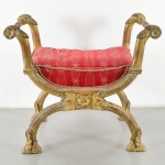 Faldistório em madeira entalhada e dourada, estilo Império, com assento estofado de formato retangular, revestido em tecido vermelho com padronagem decorativa. Estrutura com montantes laterais arqueados terminando em volutas, unidos por travessas torneadas. Base com pernas curvas em X, com caneluras longitudinais e terminação em pés estilizados, interligadas por elemento central com entalhe em motivo floral. Medidas: Alt.: 76 x Comp.: 83 x Larg.: 51 cm.