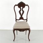 Cadeira construída em madeira nobre, estilo Dom José I, com espaldar recortado e vazado, apresentando tabela central em formato sinuoso com entalhes em volutas e elemento superior concheado. Assento estofado de formato trapezoidal, revestido em tecido de tonalidade bege com padronagem geométrica, arrematado por galão. Saia recortada com entalhe central em motivo fitomorfo. Apoio sobre quatro pernas cabriolet, com joelhos marcados e terminação em pés recurvos. Medidas: Alt.: 110 x Comp.: 42 x Larg.: 47 cm.