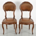 Par de cadeiras em madeira entalhada, de estilo Luís XV, com espaldar recortado em formato violinado, estruturado por montantes curvos e elemento central em concha. Assento estofado em couro, com acabamento em tachas metálicas. Cintura recortada com movimento ondulado e pernas cabriolet terminando em pés de enrolamentos. Medidas: Alt.: 100 x Comp.: 46 x Larg.: 49 cm.