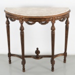 Aparador em madeira entalhada e dourada, em estilo neoclássico(Luís XVI), de formato semicircular, com tampo em mármore claro de contorno recortado, apoiado sobre cintura com friso decorado por elementos geométricos e motivos estilizados, intercalados por reservas verticais com ornatos entalhados. Saia recortada com festões e elementos fitomorfos em relevo. Apoiado sobre quatro pernas torneadas e afiladas, com elementos de transição em forma de anel e base em pés arredondados, interligadas por travessa inferior recortada, centrada por elemento torneado em forma de pináculo. Medidas: Alt.: 82 x Comp.: 86 x Larg.: 30,5 cm.