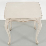 Mesa de apoio construída em madeira, estilo Luís XV, com tampo de contorno recortado e borda moldurada, saia sinuosa com elemento central em voluta e pernas cabriolet terminando em pés de enrolamento. Acabamento pintado em tom claro com pátina. Medidas: Alt.: 51 x Comp.: 51 x Larg.: 43,5 cm.