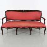 Canapé em madeira entalhada, de estilo Luís XV, com espaldar ondulado e arremate central esculpido. Assento e encosto estofados em tecido de tonalidade vermelha, fixados por tachas aparentes. Braços curvos integrados à estrutura. Saial recortado com concha central estilizada. Sustentado por seis pernas cabriolet, com joelhos proeminentes e terminação em pés de enrolamentos. Medidas: Alt.: 88 x Comp.: 171 x Larg.: 57 cm.
