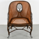 Poltrona de encosto contínuo em estrutura de madeira torneada, com assento e espaldar em palhinha natural tramada. Encosto em forma de ferradura, integrado aos braços, com montantes curvos; na região central, reserva oval contendo aplique vazado em metal com motivo fitomorfo estilizado. Braços com terminais zoomórficos em metal, representando cabeças de ave aquática, unidos a montantes frontais levemente inclinados. Cintura assentada sobre travessas e reforços em forma de varas, com amarrações simuladas, compondo arcabouço estrutural de inspiração bambu. Apoiada sobre quatro pés, sendo os anteriores com terminações metálicas em forma de garra estilizada, e os posteriores ligeiramente recuados. Apresenta perfuração na palhinha, terminações metálicas demandam restauro. Medidas: Alt.: 91 x Comp.: 69 x Larg.: 59 cm.