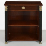 Aparador construído em madeira, em estilo Império de inspiração neoclássica, com corpo retangular, tampo superior plano com ressaltos laterais e uma gaveta na faixa frontal, provida de puxador metálico embutido. Estruturado por montantes laterais destacados(um necessita restauro), em contraste cromático, encimados por aplicações de cariátides em metal dourado, funcionando como pilastras ornamentais, e apoiados em pés de bronze com terminação zoomórfica. Caixa com interior compartimentado por prateleira fixa, formando dois vãos abertos. Medidas: Alt.: 84 x Comp.: 73 x Larg.: 31 cm.