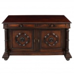 Aparador/arcaz construído em madeira, de inspiração neorrenascentista, com corpo retangular e tampo plano com leve beiral. Frente organizada em dois registros: na parte superior, duas gavetas alinhadas, com frentes almofadadas e puxadores em madeira torneada; abaixo, duas portas de abrir, cada qual composta por painel rebaixado central aplicado com reserva quadrifoliada em relevo, tendo ao centro roseta entalhada. Estrutura lateral marcada por pilastras torneadas, com bases e capitéis estilizados, apoiadas sobre plinto saliente. Base com soco moldurado assente sobre pés em forma de bola parcialmente recoberta por folhas estilizadas (tipo bola e garra estilizada). Interior compartimentado por prateleira fixa. Ferragens com entradas de chave e chaves em metal recortado. Gavetas com encaixes tipo rabo de andorinha visíveis. Apresenta pequeno destacamento da placagem do tampo. Medidas: Alt.: 82 x Comp.: 135 x Larg.: 50 cm.