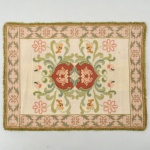 Tapete arraiolo, decoração floral estilizada, com composição central simétrica formada por ramos curvilíneos e flores, ladeada por pequenos elementos florais e cercadura com padrão repetitivo de volutas. Medidas: Comp.: 122 x Larg.: 96 cm.