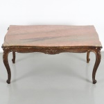 Mesa de centro em madeira, estilo Luís XV, com tampo em mármore rosa de contorno recortado, assentado sobre estrutura com borda moldurada, saia recortada e ondulada, com entalhe central em motivo fitomorfo, apoio sobre quatro pernas cabriolet, com joelhos entalhados e terminação em pés recurvos. Medidas: Alt.: 48 x Comp.: 96 x Larg.: 50 cm.
