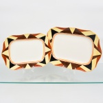 J & G Meakin, Staffordshire - Inglaterra(Fundada em 1851). Duas(02) travessas em faiança inglesa da década de 1930, padrão "SOL". Formato retangular, de quinas levemente chanfradas, bordo recortado em ondulações; esmaltação de tom marfim, dotado de rica decoração Art Déco, contendo composição geométrica radial na aba, formada por reservas triangulares alternadas em esmalte de tonalidade preta, marrom e amarelo-creme, dispostas em sequência contínua. Centro circundado por frisos concêntricos em tom laranja e mostarda, este último se replica no contorno da borda. Marca da manufatura no verso. Medidas: Comp.: 31 x Larg.: 22 cm; Comp.: 36 x Larg.: 26 cm. Estado de conservação conforme fotografias. Apresentam desgastes pontuais de uso, vide foto.