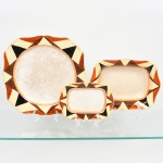 J & G Meakin, Staffordshire - Inglaterra(Fundada em 1851). Duas(02) travessas(uma funda e uma rasa) e um(01) prato de serviço em faiança inglesa da década de 1930, padrão "SOL". Formatos retangular e quadrangular, de quinas levemente chanfradas, bordo recortado em ondulações; esmaltação de tom marfim, dotado de rica decoração Art Déco, contendo composição geométrica radial na aba, formada por reservas triangulares alternadas em esmalte de tonalidade preta, marrom e amarelo-creme, dispostas em sequência contínua. Centro circundado por frisos concêntricos em tom laranja e mostarda, este último se replica no contorno da borda. Marca da manufatura no verso. Medidas: Travessas: Alt.: 5,5 x Comp.: 26 x Larg.: 19 cm; Comp.: 19,5 x Larg.: 14 cm. Prato de serviço: Diam.: 30 cm. Estado de conservação conforme fotografias. Apresentam manchas do tempo e desgastes pontuais de uso, vide foto.