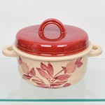 S.I.C. (Scuola Italiana Ceramica), Casale Monferrato - Itália. Elegante caçarola em majólica italiana da década de 1950/60; esmaltação vítrea de tonalidade creme, decorado com composição botânica manual em tom bordô, tampa circular removível integralmente na mesma tonalidade,  puxador e alças laterais em arco. Marca da manufatura ao fundo. Medida: Alt. 17,5 x Comp.: 28 x Larg.: 22 cm.