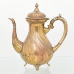 Bule para café confeccionado em metal amarelo, bojo moldado com frisos em espiral, assente sobre três pés de espátula, tampa campaniforme, dotada de abertura basculante, encimada por puxador ovoide, bico vertedor curvilíneo, alça lateral em voluta. Apresenta sinais de oxidação e desgastes. Medidas: Alt.: 25 x Comp.: 23 x Larg.: 13 cm.