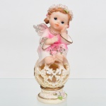 Escultura em resina moldada e policromada, representando figura de anjo infantil, apoiada sobre esfera vazada com composição floral, com base circular integrada. Traja veste com aplicação de relevos florais e detalhes em douração. Asas posteriores com policromia em tons claros. Medidas: