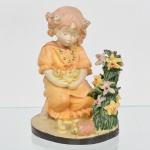 Escultura em resina moldada e policromada, representando figura infantil em composição campestre, em posição sentada, trajando vestido com modelagem em pregas, portando aves no colo. Composição com elementos vegetalistas em relevo e base circular integrada, com presença de pequenos animais. Medidas: