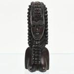 Escultura em madeira representando busto feminino estilizado, de inspiração africana, com traços geometrizados, penteado em tranças segmentadas; composição associada a repertórios formais da África Ocidental, sem atribuição específica. Medidas: