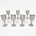 Conjunto de cálices confeccionados em estanho, bojo cilíndrico, fuste torneado base campaniforme. Produção nacional da região de MG. Composto de sete(07) unidades. Medidas: