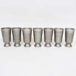 Conjunto de copos confeccionados em estanho, bojo aproximadamente obcônico apoiado base circular elevada. Produção nacional da região de MG. Composto de sete(07) unidades. Medidas: