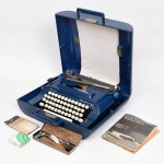 Máquina de escrever de mesa, modelo Remington 10, fabricada pela Sperry Rand, com corpo em metal esmaltado em tonalidade azul, teclado alfanumérico com teclas em material plástico moldado, carro móvel com régua graduada e alavanca de retorno lateral. Sistema de impressão por barras de tipos, com fita bicolor em carretéis superiores. Acompanha estojo rígido em material plástico moldado com alça integrada e fecho frontal, manual de instruções impresso, cartão e conjunto de ferramentas e acessórios acondicionados em estojo metálico. Sem garantias de funcionamento. Medidas: Alt.: x Comp.: x Larg.: