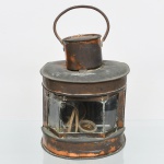 Lanterna em cobre e/ou latão, com estrutura metálica e painéis de vidro planos. Parte superior com chaminé cilíndrica e alça móvel em arco. Base anelar e porta posterior articulada para acesso ao interior. Peça originalmente destinada a iluminação a combustível (óleo/querosene), posteriormente adaptada para uso elétrico, conforme presença de soquete e fiação. No estado, conforme fotografias. Medidas: