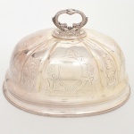 Cloche (cobertura de serviço) para carne/assados confeccionado em metal prateado, formato oblongo de perfil abaulado, moldado com frisos verticais e campos gravados com cartelas rocaille e volutas; pega superior fundida em forma de golfinhos afrontados, com texturização de escamas e base circular perlada em relevo, obtidos através da técnica do cinzelado; bordo inferior com filetes concêntricos. Ausência de marca de manufatura. Medidas: Alt.:23,5 x Comp.: 36 x Larg.: 26 cm. Apresenta pequenos desgastes isolados no banho de prata(sangria), necessita polimento.