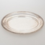FRACALANZA. Elegante bandeja confeccionada em metal espessurado à prata, formato oval, centro ligeiramente rebaixado, borda relevada com fileira de frisos intercaladas por fitas cruzadas, ornato obtido através da técnica do cinzelado. Marca da manufatura no verso. Medidas: