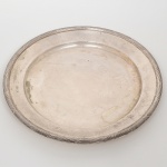 FRACALANZA. Elegante bandeja confeccionada em metal espessurado à prata, formato circular, centro ligeiramente rebaixado, borda relevada com fileira de frisos intercaladas por fitas cruzadas, ornato obtido através da técnica do cinzelado. Marca da manufatura no verso. Medidas: