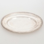 FRACALANZA. Elegante bandeja confeccionada em metal espessurado à prata, formato oval, centro ligeiramente rebaixado, borda relevada com fileira de frisos intercaladas por fitas cruzadas, ornato obtido através da técnica do cinzelado. Marca da manufatura no verso. Medidas: