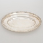 FRACALANZA. Elegante bandeja confeccionada em metal espessurado à prata, formato oval, centro ligeiramente rebaixado, borda relevada com fileira de frisos intercaladas por fitas cruzadas, ornato obtido através da técnica do cinzelado. Marca da manufatura no verso. Medidas: