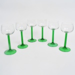 Conjunto de taças em vidro incolor com haste de tonalidade verde; bojo hemisférico em vidro incolor, com transição para haste cilíndrica em vidro verde translúcido, terminando em base circular no mesmo tom. Composto de seis(06) unidades. Medidas: