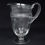 Belíssima jarra executada em cristal europeu, diáfano e incolor; bojo oval alongado, bico vertedor ondulado e revirado para fora, alça lateral curvada e aplicada sobre a superície, fuste em anel sobre base circular; ricamente gravado com flores e faixa contínua de motivo vegetalista. Medidas: Alt.: x Diam.: