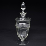 Belíssima licoreira executada em cristal europeu, diáfano e incolor; bojo oval alongado, fuste em anel e base circular, gargalo evertido, tampa de formato ovoide facetado; ricamente gravado com flores e faixa contínua de motivo vegetalista. Medidas: Alt.: x Diam.: