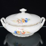 Springer & Co, EPIAG - Checoslováquia(Fundada entre 1918 e 1920 a partir de fábricas nos arredores de Carlsbad). Excepcional terrina com tampa em porcelana tcheca da década de 1920. Esmaltagem vítrea na cor branca, bojo elipsoide assentado sobre base circular moldada com movimento ondulatório, bordas do bojo e da tampa  circundada por faixa contendo frisos e enrolamentos relevados na própria pasta; decorada com bela composição botânica em estampagem policromada, predominando as tonalidades amarelo, ocre, azul, coral, verde e marsala, distribuídas nas faces do bojo e na tampa; contornos ornamentados com aplicação de filetes em douradura; tampa ligeiramente abaulada, encimada por puxador com feitio de pião, alças laterais reviradas para cima. Marca da manufatura no verso. Medidas: Alt.: 14 x Comp.: 27 x Larg.: 22 cm. (A Springer & Co de Elbogen na Boêmia foi formada na década de 1880 e encerrou suas atividades em 1945. Ela foi uma das fábricas fundadoras originais da OEPIAG (mais tarde EPIAG), que era uma associação de olarias formadas pelo governo de Viena em 1918 para promover a venda de cerâmica e porcelana da Boêmia. Foi inicialmente denominado OEPIAG, um acrônimo para Österreichische Porzellan Industrie AG ou Austrian Porcelain Industry, mas foi alterado para EPIAG - Erste Böhemische Porzellan Industrie AG que significa Primeira Indústria de Porcelana da Boêmia - em 1920 após a independência da Checoslováquia).